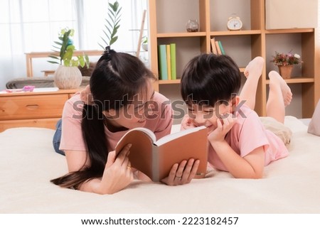 Asian happy elementary school kid and single mom spend free time reading a book and tease in holiday. Beautiful mother telling fairy tale stories to adorable son laying on bed, parenthood relationship