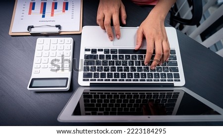 A young financial market analyst works in the office on his laptop while sitting at a wooden table. Businessman analyzing documents in hand Graph and Finance Accounting Concepts