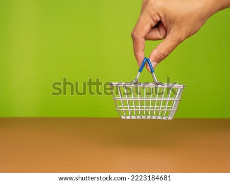Hand holding a mini shopping cart with a green background. Concept of shopping online. Close-up photo