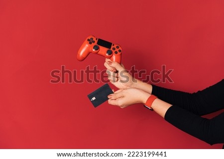 Gamepad and credit card in female hand against red background.