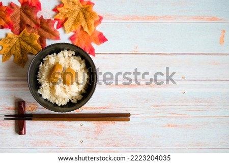Left-leaning photo of chestnut rice with chopsticks and autumn leaves and wooden background