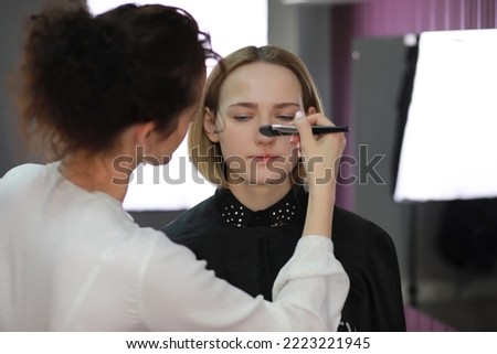 Young girl with a make-up artist in the studio in front of a mirror
