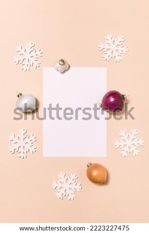 Christmas ornaments made of onions and garlic with snowflakes and white paper card on a pastel beige background. Happy New Year's gift card and vegetable concept. Flat lay.