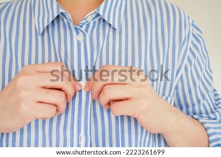 hands fasten button the blue and white striped shirt , represent the concept of getting the first button right and all the others will be in line, selective focus on the tip of the finger Royalty-Free Stock Photo #2223261699