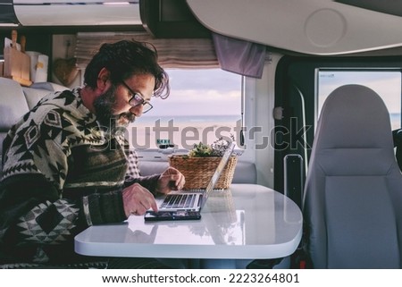 Working off grid in alternative office and online job lifestyle concept man. Adult people work on a laptop inside a camper van motor home. Smart working in travel vehicle transport. Using notebook Royalty-Free Stock Photo #2223264801