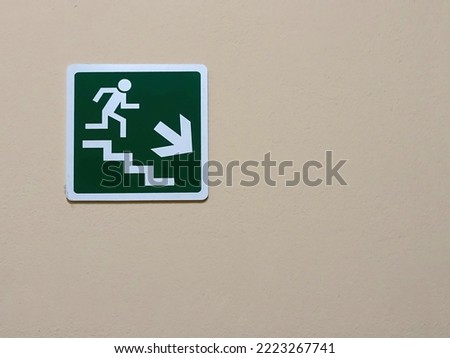 Green sign down the stairs on a bright wall. Direction to the emergency exit