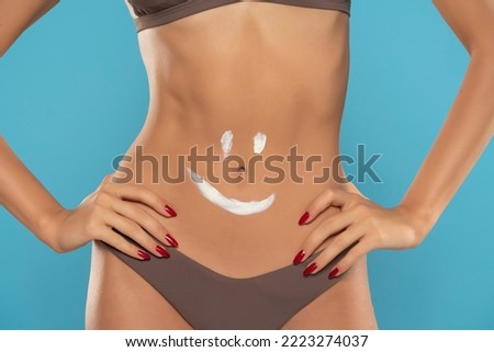 Woman's belly close-up with smile drawn with lotion on a blue studio background