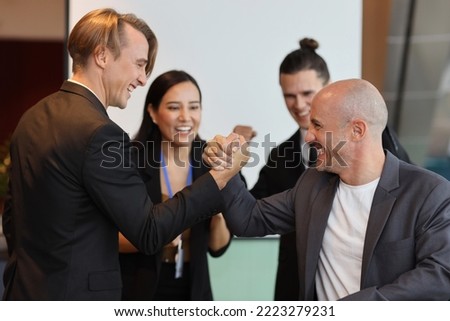 Young multiethnic collaborative process of professional businesspeople arm wrestling after new business contract signed with happy smiling face. Coworker and working together concept
