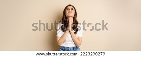 Woman pleading, begging and looking up desperate, need help, standing over beige background.