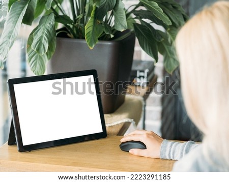 Distance work. Digital mockup. Online connection. Unrecognizable woman sitting desk working tablet computer blank screen using mouse in light room interior.