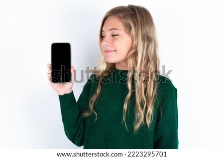Photo of interested caucasian teen girl wearing green knitted sweater over white background hold telephone look side empty space screen