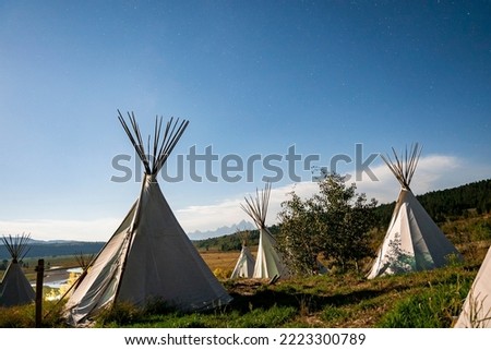 View of teepees on grassy field with blue sky in background. Tents for camping on landscape during summer. Adventure in nature at famous Yellowstone National Park.
