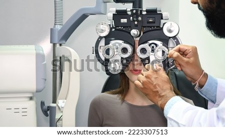 Young woman looking through optical phoropter, checking eye vision with optometrist specializing in clinic