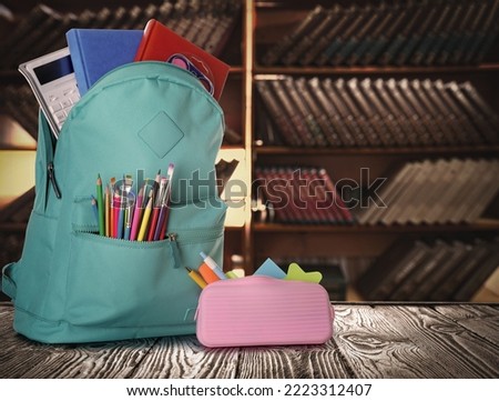 Backpack with school stationery on wooden table in library, space for text