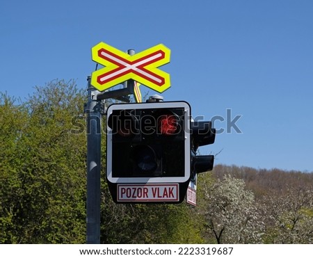 The inscription in Czech - Attention train. Railroad crossing with closed barrier and passing train in Prague, Czech Republic. Railroad crossing barrier with semaphore for warning signals.
