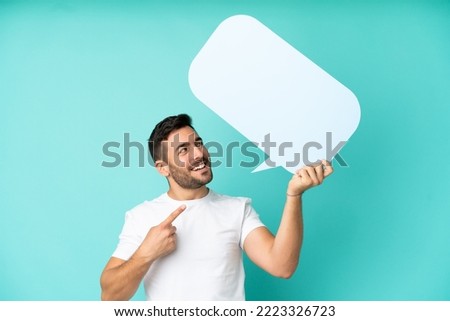Young handsome caucasian man isolated on blue background holding an empty speech bubble and pointing it Royalty-Free Stock Photo #2223326723