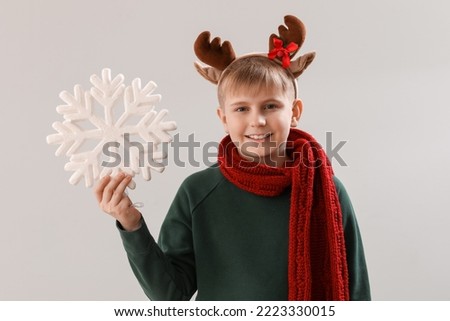 Happy little boy in reindeer horns with snowflake on light background