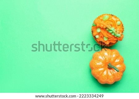 Tasty Halloween cupcake and pumpkin on green background