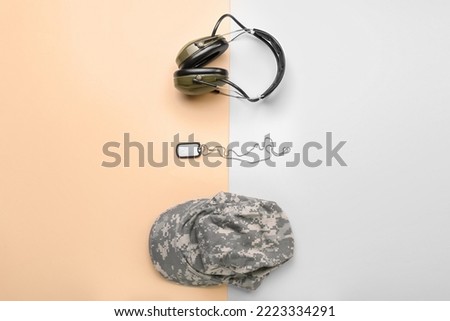 Military cap, tag and headphones on color background