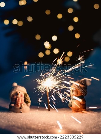 Merry Christmas. New Year's card Sparkler in the snow in the evening. two decorative figures a snowman and a bear in the snow outdoors
