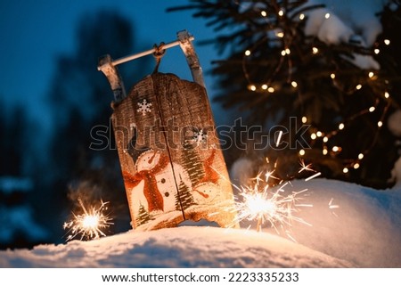 Merry Christmas. New Year's card Sparkler in the snow in the evening. wooden decorative sled with a snowman pattern in the snow outdoors