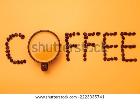 Black coffee in a cup with coffee beans making coffee text on yellow background, close-up.
