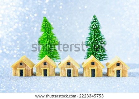 Row of miniature houses placed in front of two toy Christmas trees on glittering background.