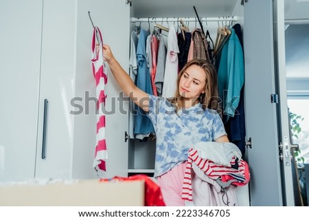 Woman selecting clothes from her wardrobe for donating to a Charity shop. Decluttering, Sorting clothes and Cleaning Up. Reuse, second-hand concept. Conscious consumer, sustainable lifestyle. Royalty-Free Stock Photo #2223346705
