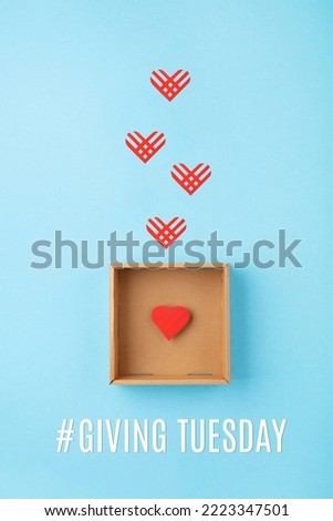 Giving Tuesday, global day of charitable giving after Black Friday shopping day. Charity, give help, donations support concept. Empty brown box and red paper hearts on blue background. Top view.