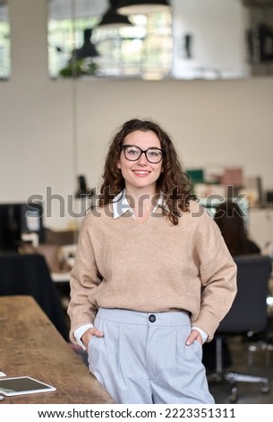 Young happy smiling pretty professional business woman at workplace, female company office worker, entrepreneur or businesswoman executive standing in office, looking at camera, vertical portrait. Royalty-Free Stock Photo #2223351311