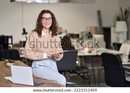 Smiling pretty young professional business woman corporate manager, female employee worker holding digital tablet computer fintech technology at workplace in modern office looking at camera.