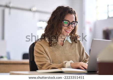 Young happy professional business woman worker employee sitting at desk working on laptop in corporate office. Smiling female student using computer technology learning online, doing web research. Royalty-Free Stock Photo #2223351451