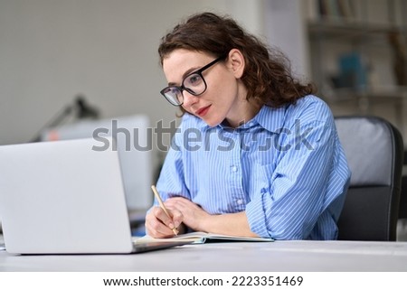 Young business woman employee using laptop writing notes, having remote virtual work conference meeting call in office or watching webcast online webinar training web course, doing research. Royalty-Free Stock Photo #2223351469