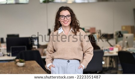 Young happy smiling pretty professional business woman at workplace, female company office worker, entrepreneur or businesswoman executive standing in office, looking at camera, portrait. Royalty-Free Stock Photo #2223351487