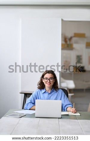 Young happy business woman company employee sitting at desk working on laptop. Smiling female professional worker or student using computer in corporate office looking at camera. Vertical portrait Royalty-Free Stock Photo #2223351513