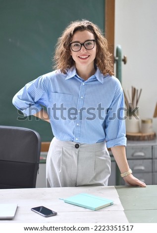 Young happy woman school professional teacher, female instructor coach standing at desk in front of chalkboard in classroom working in office presenting business education training, vertical portrait. Royalty-Free Stock Photo #2223351517