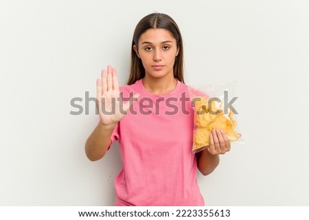 Young Indian woman holding crips isolated on white background standing with outstretched hand showing stop sign, preventing you.