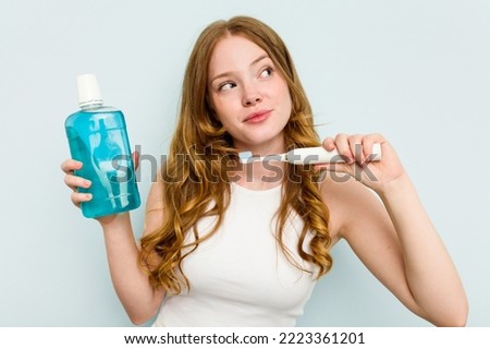 Young caucasian woman holding a mouthwash and toothbrush isolated on blue background Royalty-Free Stock Photo #2223361201
