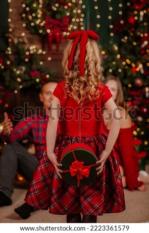Young happy family of three in red winter clothes are posing in Christmas room with tree and presents. Holiday concept.Focus is at the girl. View from the back Royalty-Free Stock Photo #2223361579