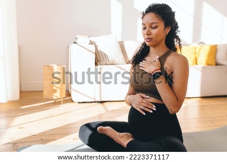 African american pregnant girl sitting on mat with closed eyes, breathing deeply, practicing yoga and pranayama techniques putting hands on chest and belly, preparing body for childbirth Royalty-Free Stock Photo #2223371117