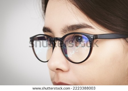 The reflection of the traders market charts in the glasses of a woman looking at a computer monitor on light background. High quality photo