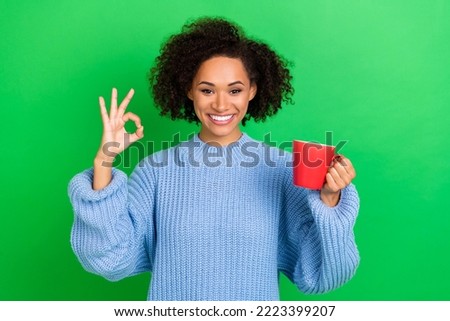 Photo portrait of nice young girl curly hair show okey beverage approval wear trendy knitwear pullover isolated on green color background