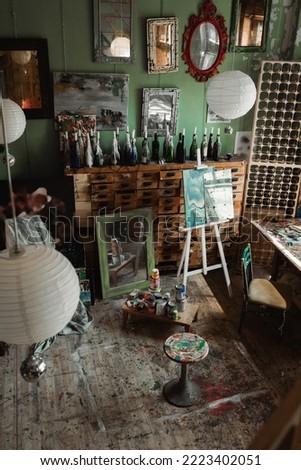 art studio with vintage furniture and mirrors with paintings on wall near easel and cans with paints