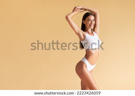 Wellness concept. Portrait of happy lady with slim sporty figure posing in underwear with hands raised up, standing over beige studio background, panorama, copy space