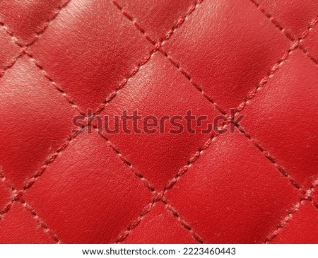 Red imitation leather with a small grainy print and a geometric print of squares, in the sun (macro, top view, texture). Royalty-Free Stock Photo #2223460443