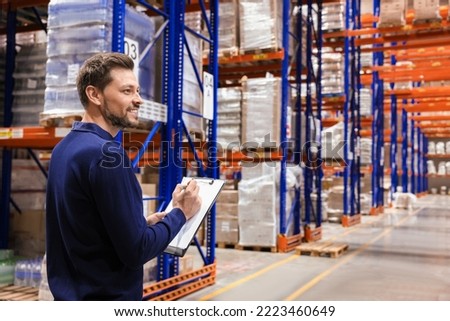 Happy manager holding clipboard in warehouse with lots of products. Space for text Royalty-Free Stock Photo #2223460649