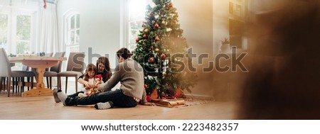 Family sitting near Christmas tree opening gift boxes. Young couple helping their daughter open Christmas gifts.
