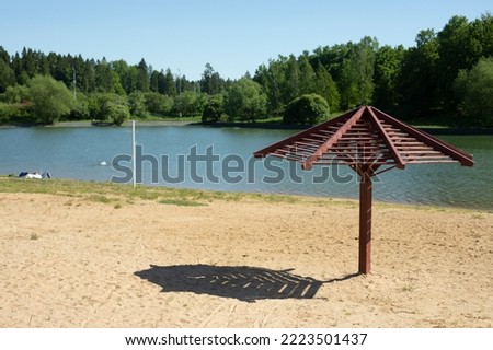 Beach on lake. Sand on shore. Place to relax. Beach without people. Umbrella from sun on shore. Wooden canopy from heat.