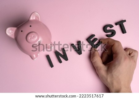 A man's hand puts together the word from the letters "invest" next to a piggy bank, close-up top view, a creative concept on the topic of business development.