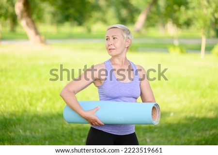 Middle-aged woman in sportswear doing in the park after a workout, smiling and holding a fitness mat, leading a healthy lifestyle.Time to sport. The concept of a healthy lifestyle, leisure.